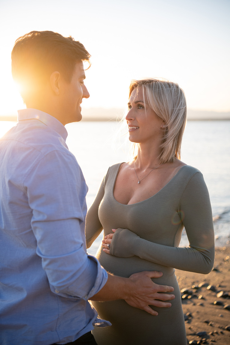 The golden hour light skims across a couple with their hands on her belly announcing their first child is on the way.